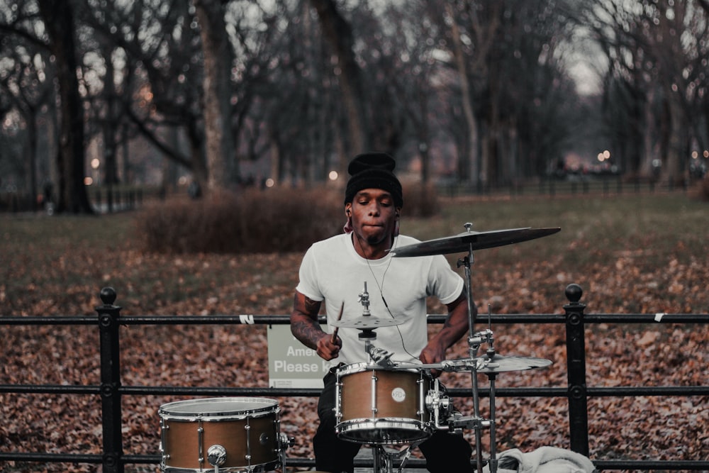 man in white crew neck long sleeve shirt and black cap standing beside drum set during
