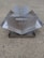 A metallic, foldable structure with serrated edges and a central cut-out design, placed on a concrete surface. The structure appears to have handles and symmetrical sides.