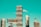A cityscape featuring modern high-rise buildings under construction, with a prominent billboard advertisement in the foreground. A construction crane is visible, indicating urban development. The sky is a clear turquoise, adding a striking backdrop to the scene.