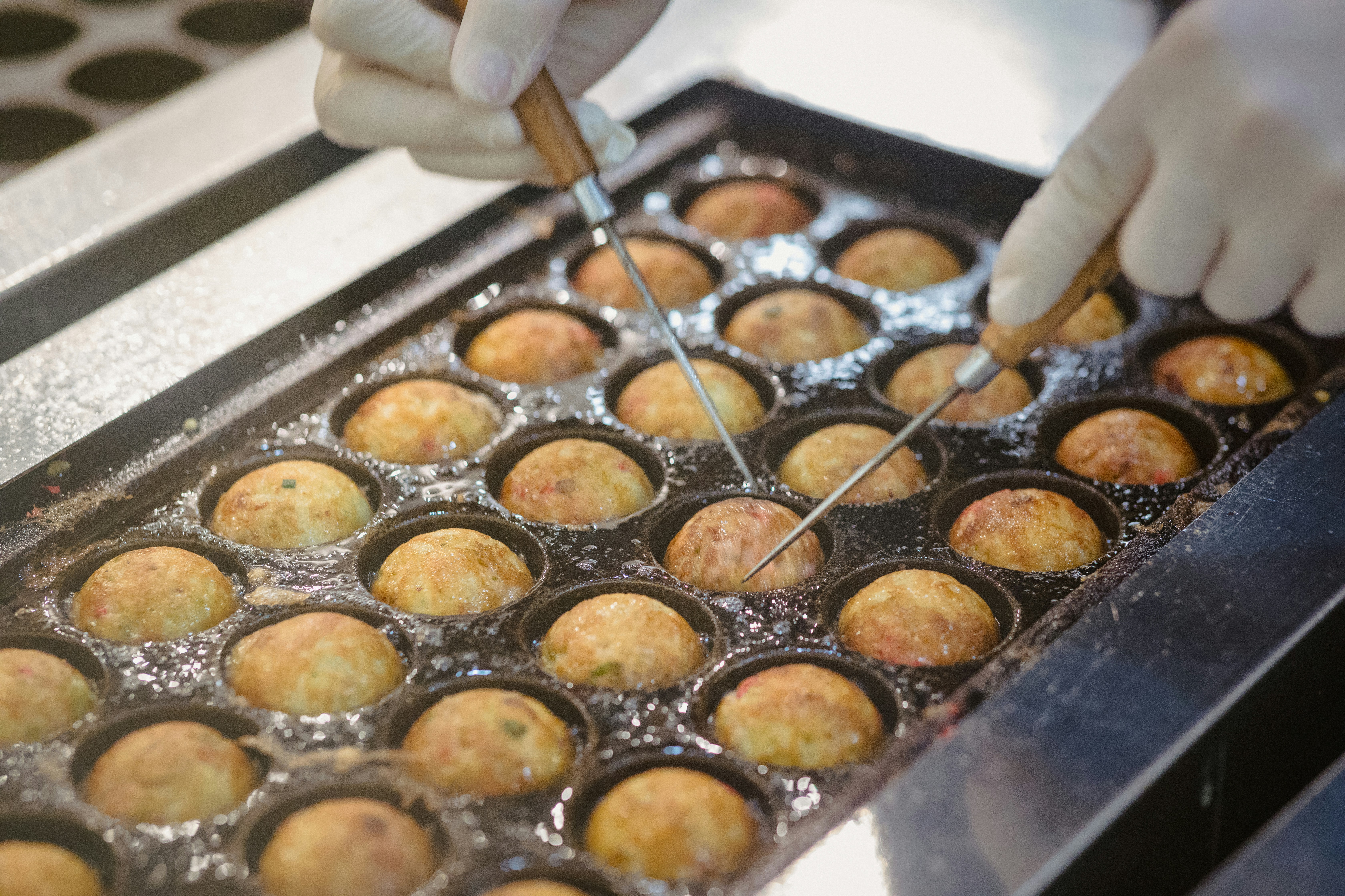 Gloved hand turning takoyaki in a cast iron pan