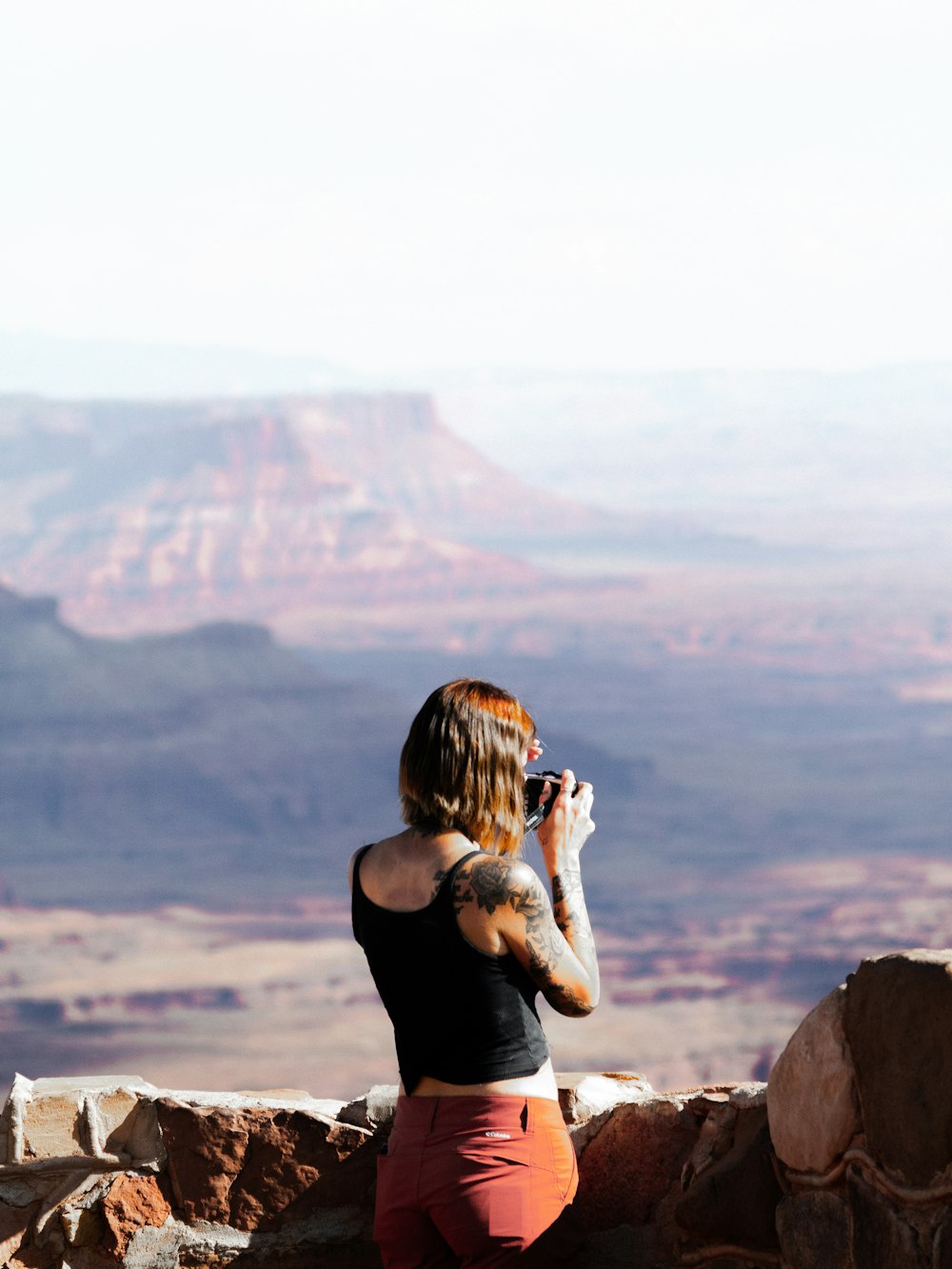 Mujer en camiseta sin mangas negra sentada en la formación rocosa durante el día