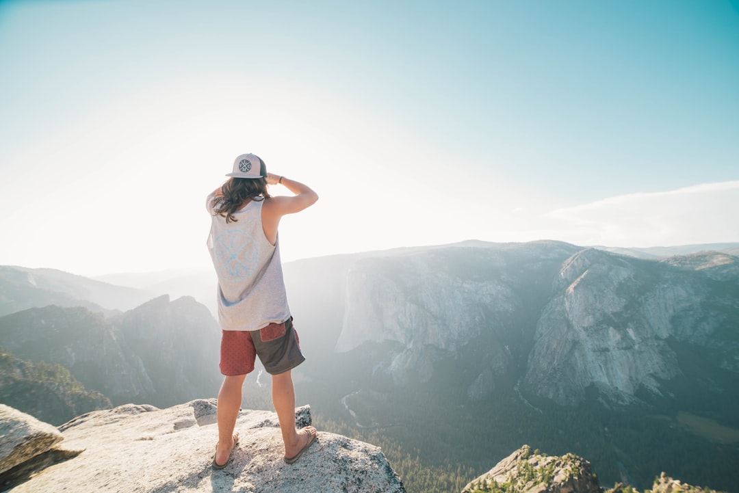 man in white t-shirt and blue shorts standing on cliff during daytime