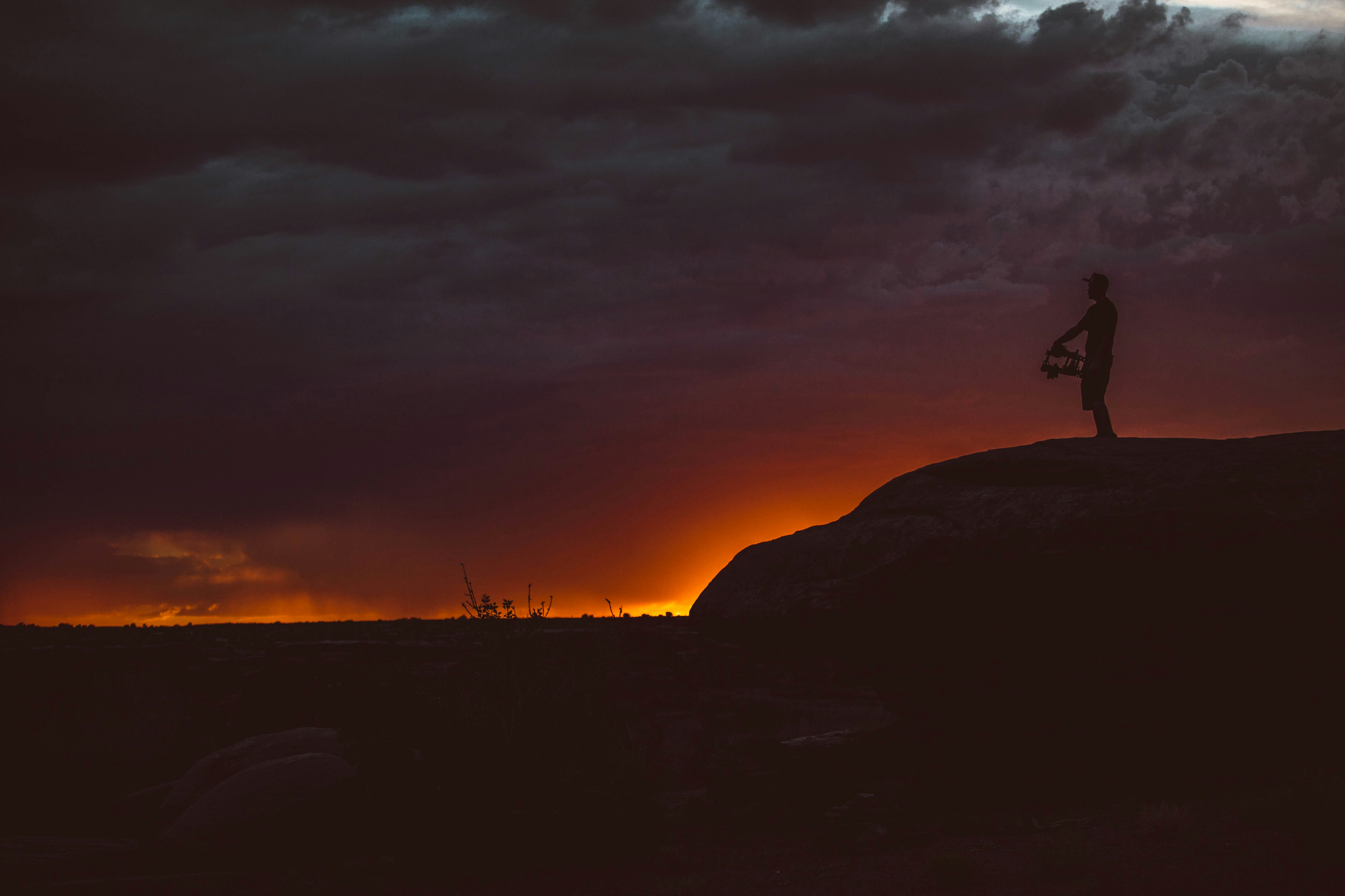 silhouette of person standing on rock during sunset