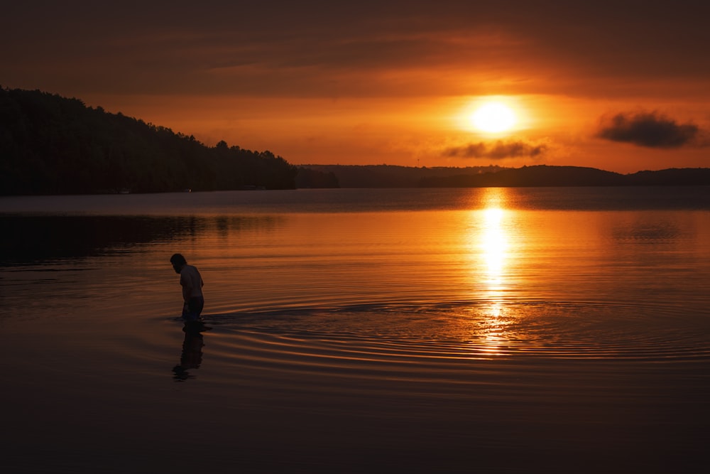 silhouette of person standing on body of water during sunset