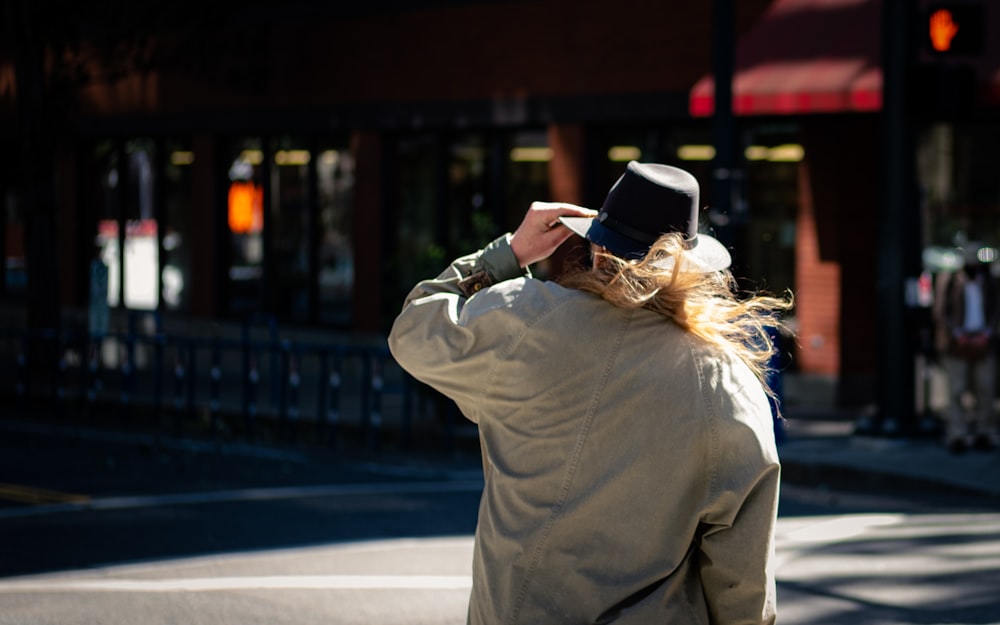 woman in gray coat and black hat standing on sidewalk during daytime