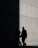 Two people in suits are walking alongside a concrete wall, with a section of the wall sharply divided between light and shadow, creating a dramatic contrast.