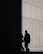 Two people in suits are walking alongside a concrete wall, with a section of the wall sharply divided between light and shadow, creating a dramatic contrast.