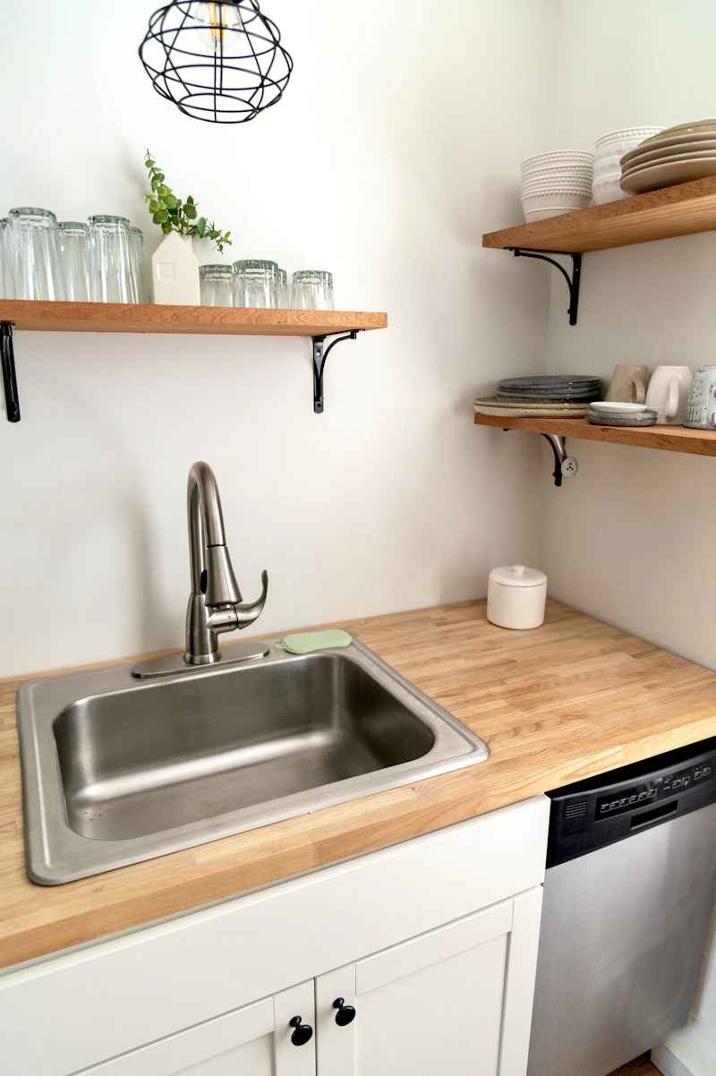 Stainless steel gooseneck faucet over a clean kitchen sink with butcher-block counter