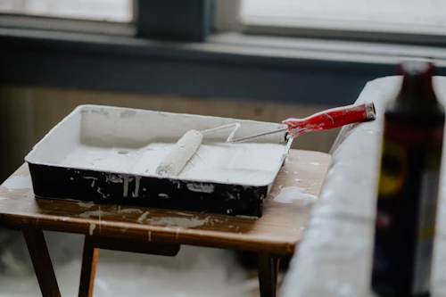Paint roller resting in a tray of white paint