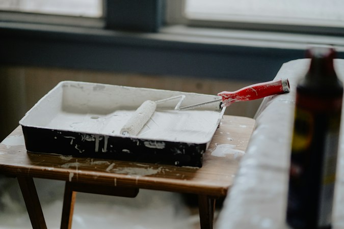 Paint roller with a red handle resting in a tray of fresh white paint, a reminder that new paint can cover older problems in a flipped home