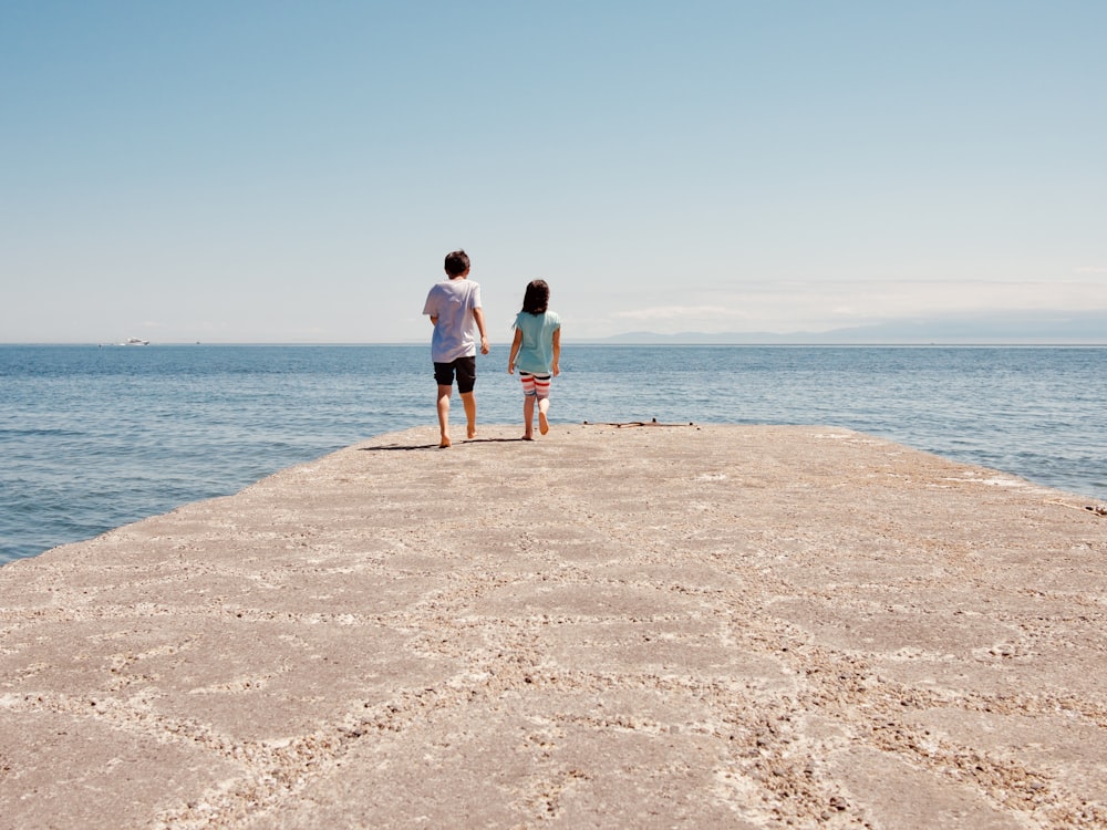 man and woman standing on brown rock near body of water during daytime