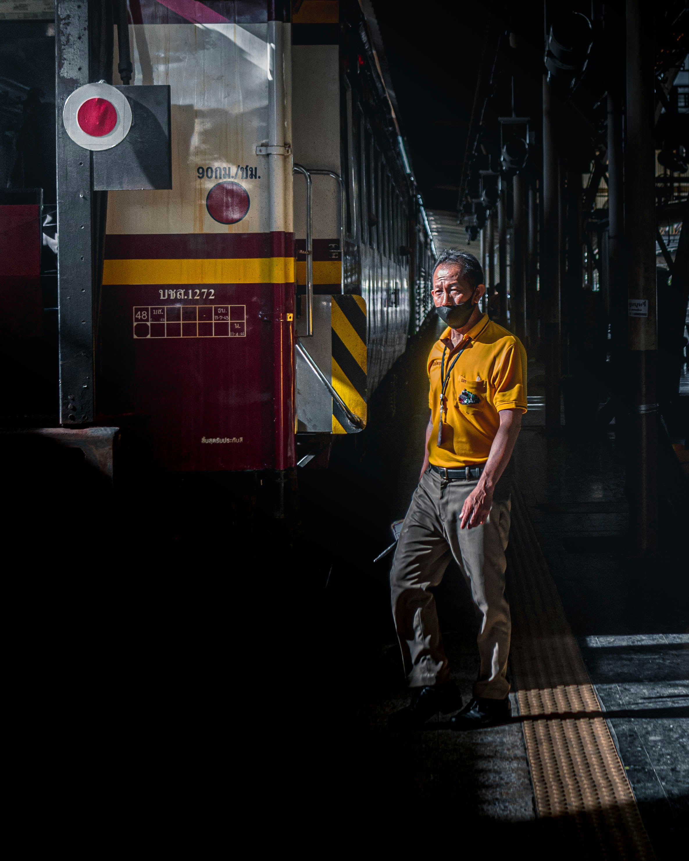 man in yellow polo shirt and white pants standing on train station