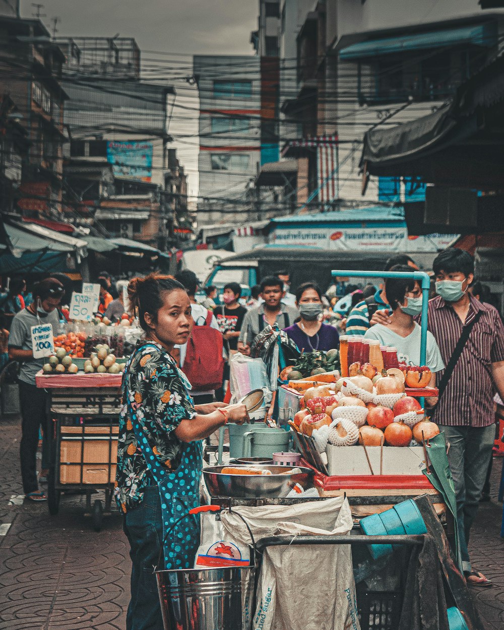 woman in blue and red floral dress standing in front of fruit stand