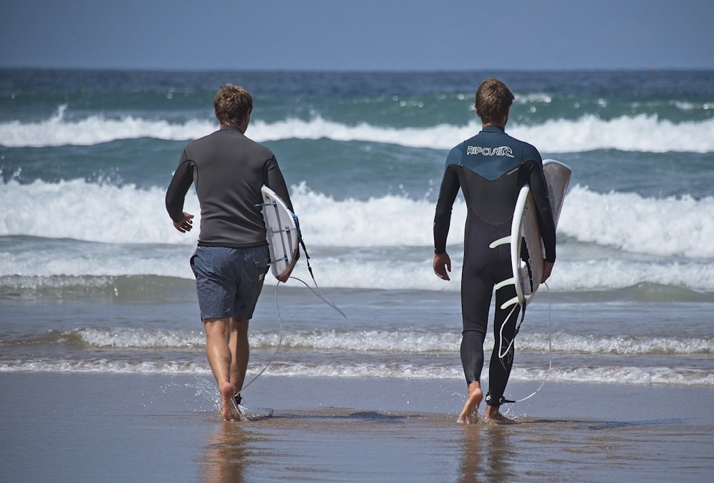 man in black and white wet suit holding woman in black and white wet suit walking