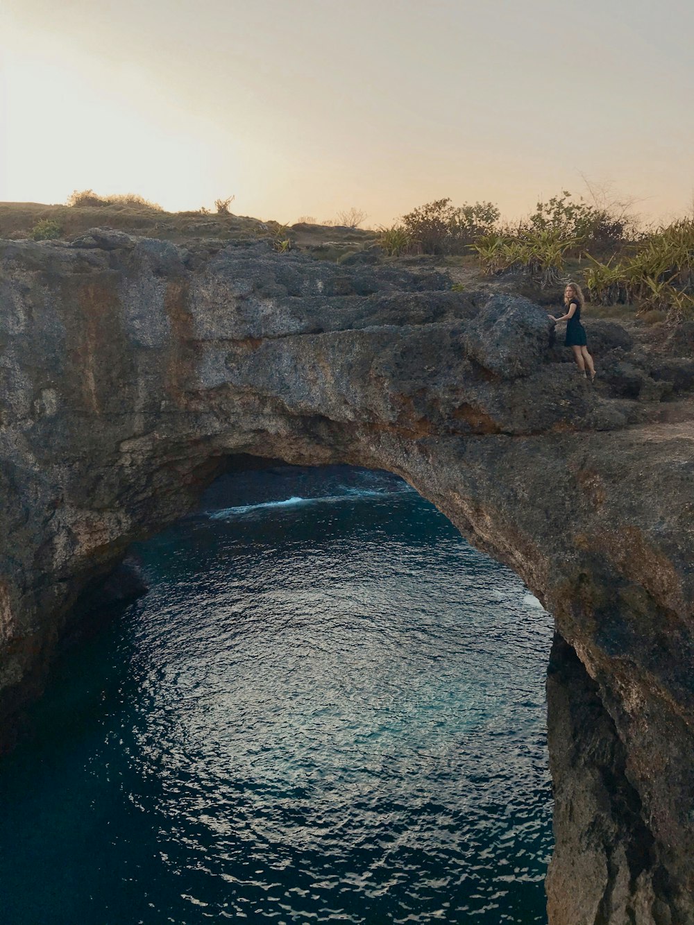 person in black shorts standing on rock formation near body of water during daytime