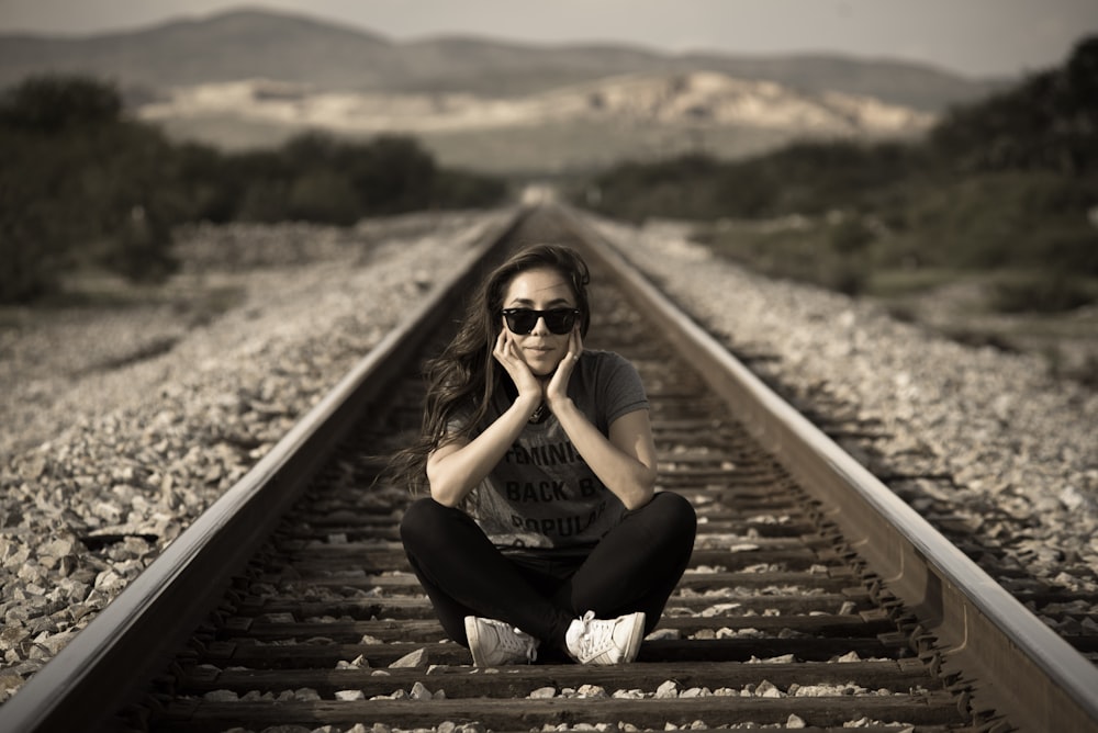 woman in black tank top and black pants sitting on train rail during daytime