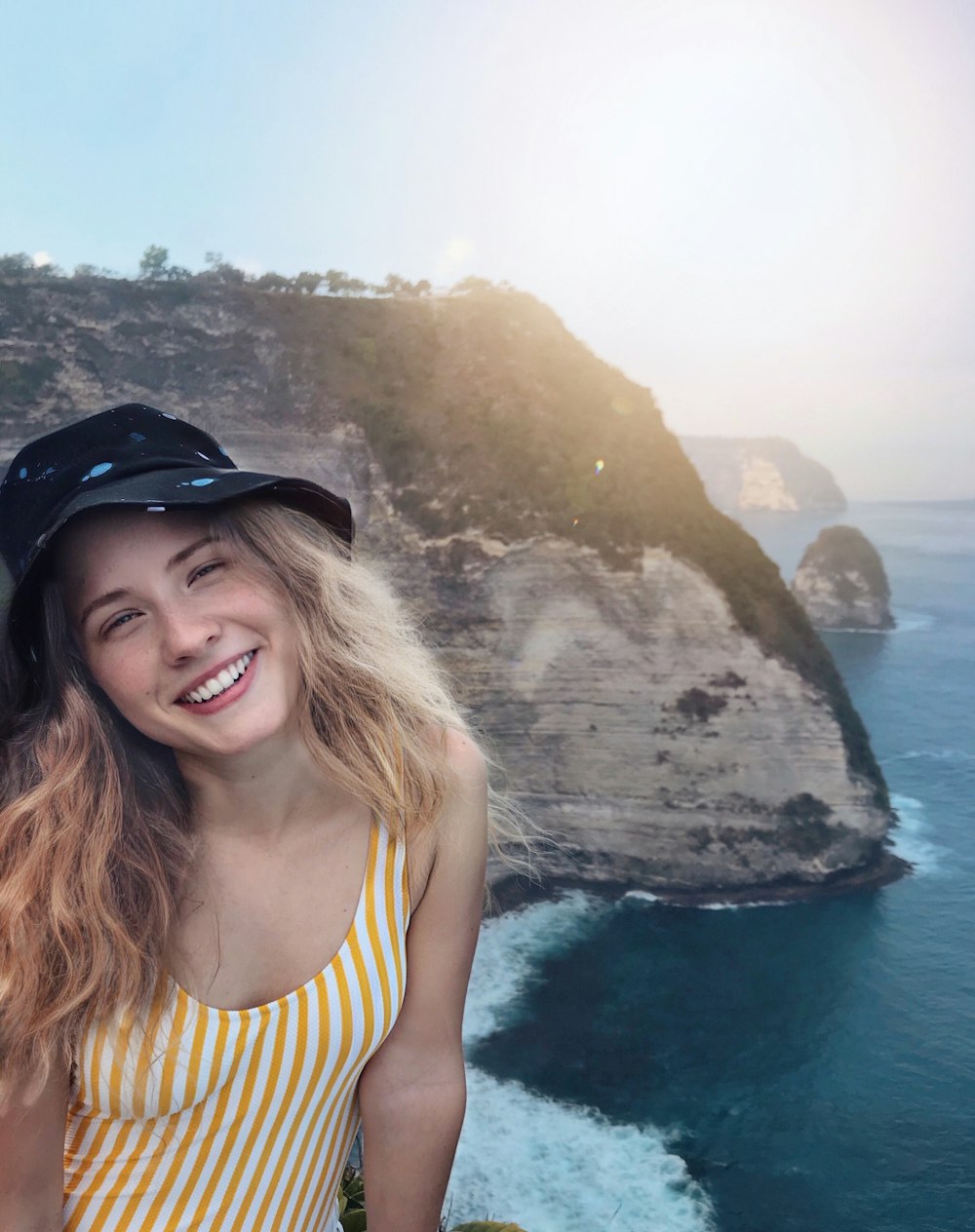 woman in yellow and black stripe tank top wearing black hat standing on rock formation during