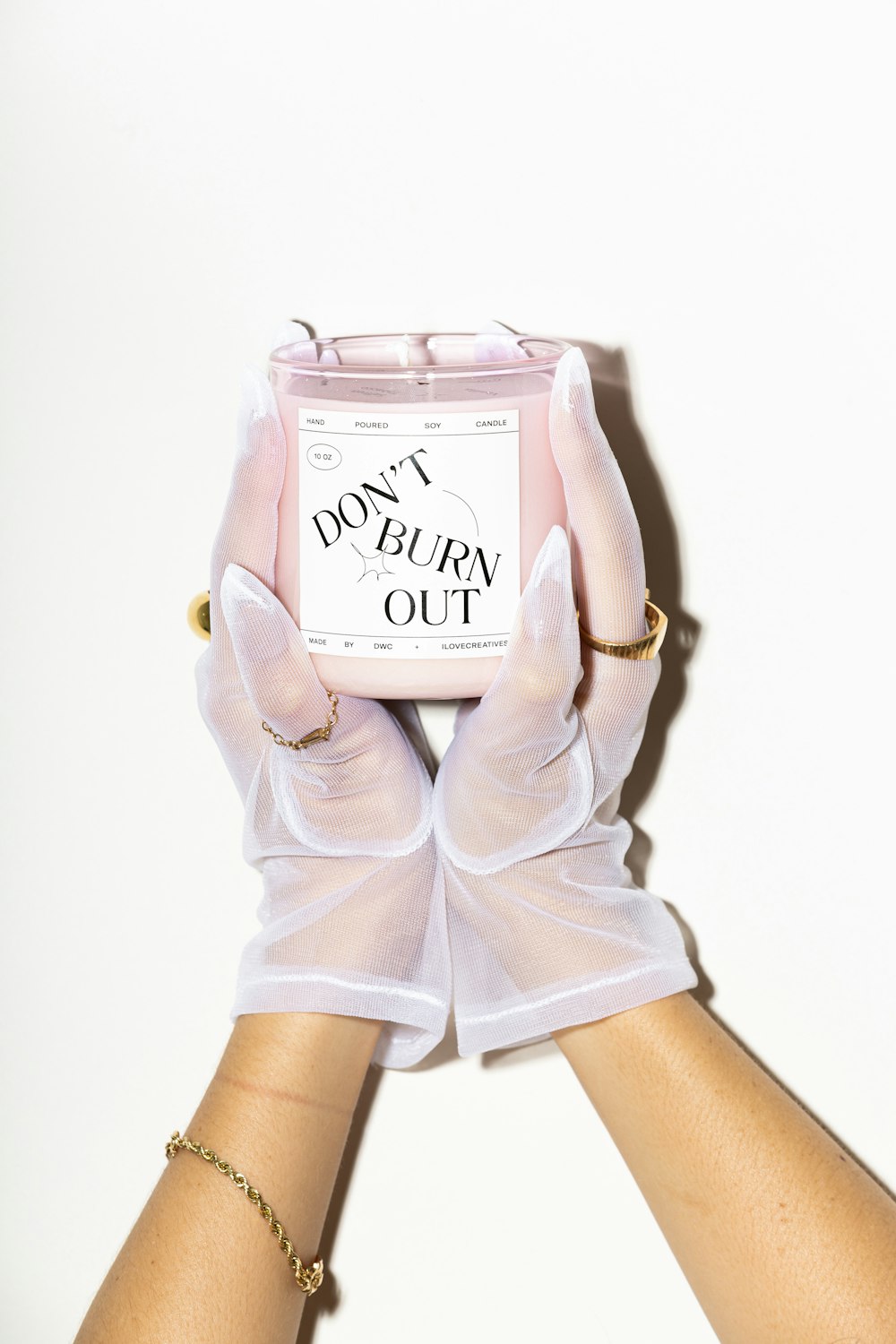 two hands in white gloves holding a pink candle