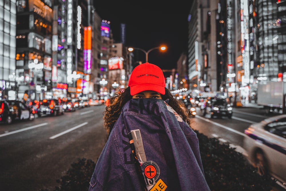 person in red knit cap and blue jacket standing on road during night time