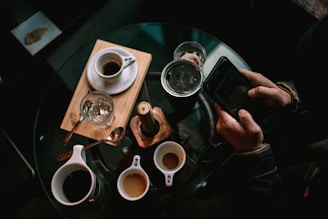 person holding black smartphone near white ceramic mug on table
