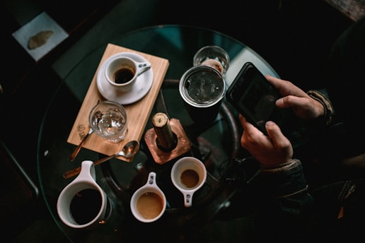 person holding black smartphone near white ceramic mug on table