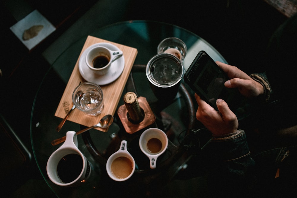 person holding black smartphone near white ceramic mug on table