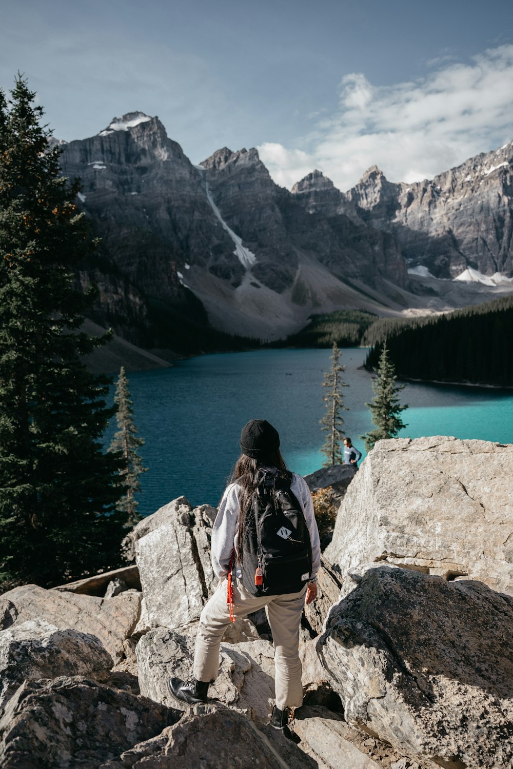 woman in black and white jacket sitting on rock near lake during daytime