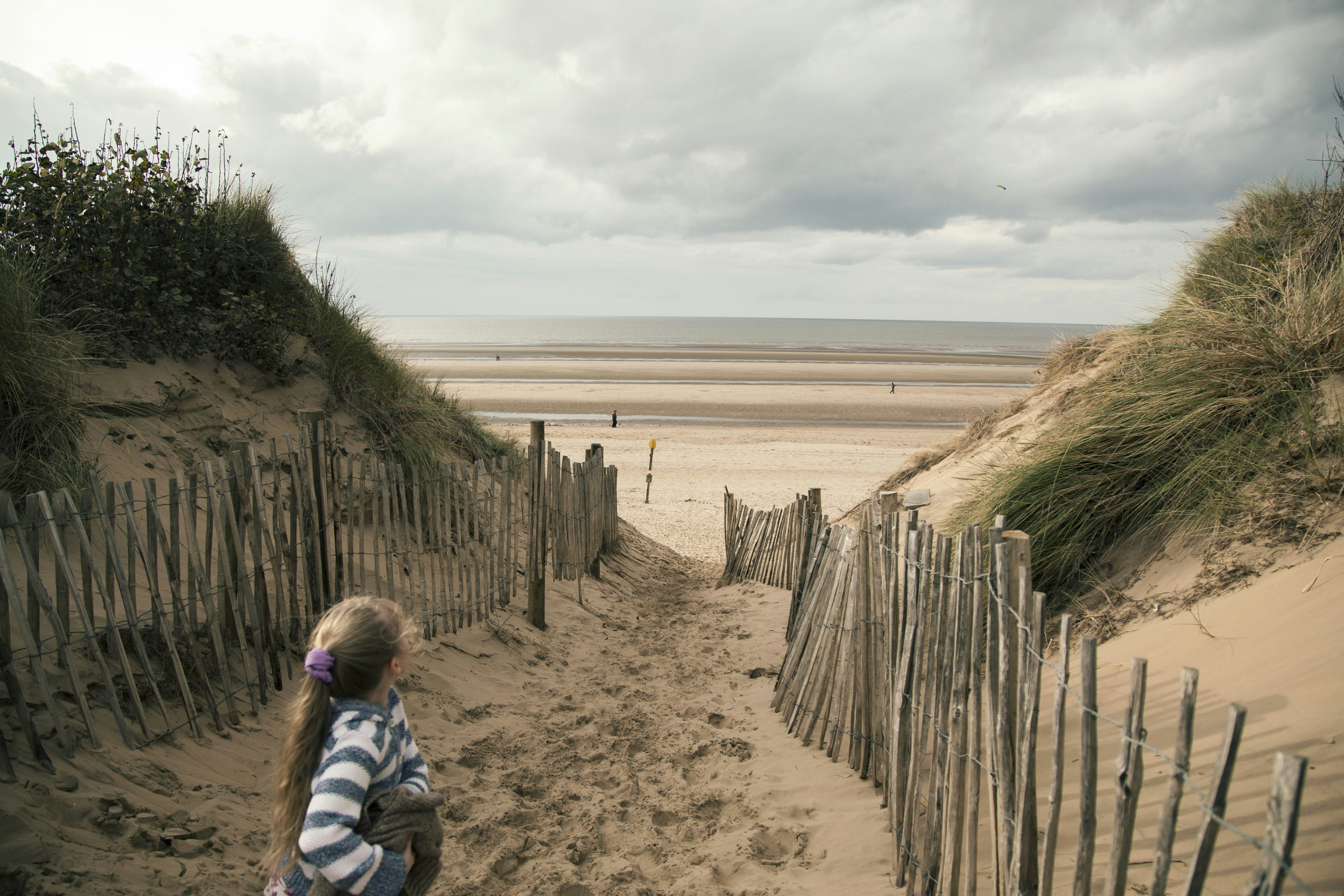 woman in blue and white striped long sleeve shirt sitting on brown sand near body of near near near near