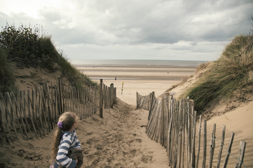 woman in blue and white striped long sleeve shirt sitting on brown sand near body of near near near near