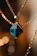 Close-up of a delicate gold necklace with a sparkling diamond pendant on a black velvet background.