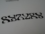 Black symmetrical shapes are printed on a white background, resembling a stylized word or pattern with artistic font design.