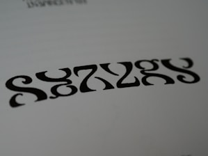 Black symmetrical shapes are printed on a white background, resembling a stylized word or pattern with artistic font design.