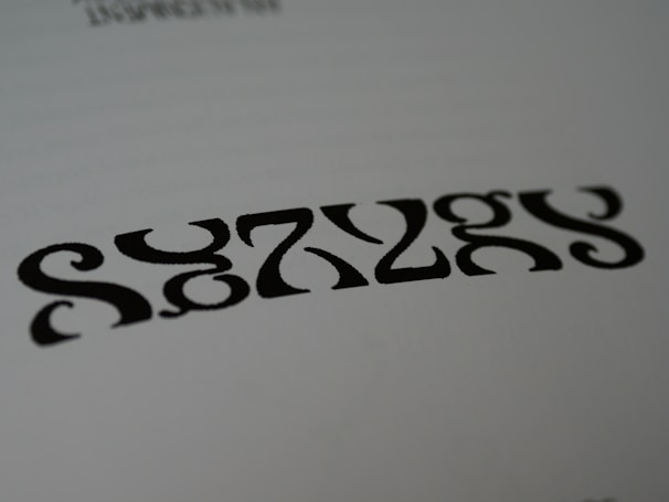 Black symmetrical shapes are printed on a white background, resembling a stylized word or pattern with artistic font design.