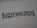 A close-up of the word 'Astronomy' written in a stylized font, resembling calligraphy. The text is black on a white background, with small star-like accents near the letters.