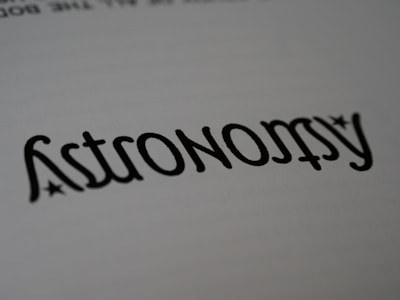 A close-up of the word 'Astronomy' written in a stylized font, resembling calligraphy. The text is black on a white background, with small star-like accents near the letters.