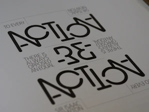 Text appears in a stylized geometric font with the words 'ACTION' and 'REACTION' prominently visible. The phrase 'TO EVERY ACTION THERE IS ALWAYS OPPOSED AN EQUAL REACTION' is included in a smaller, simpler font. The layout is minimalist with a monochromatic color scheme.