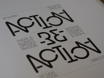 Text appears in a stylized geometric font with the words 'ACTION' and 'REACTION' prominently visible. The phrase 'TO EVERY ACTION THERE IS ALWAYS OPPOSED AN EQUAL REACTION' is included in a smaller, simpler font. The layout is minimalist with a monochromatic color scheme.