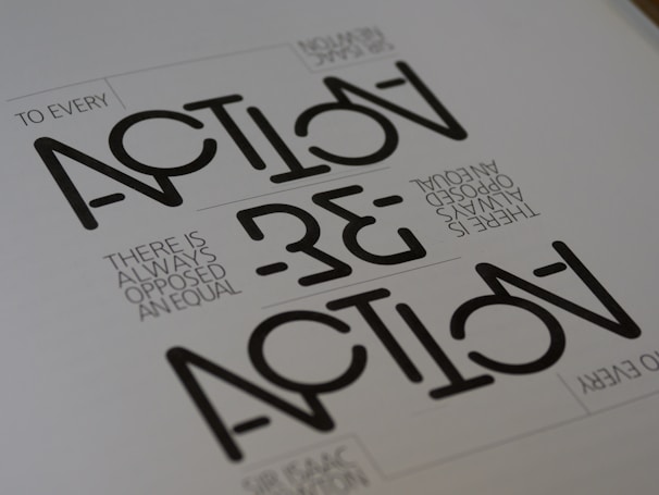 Text appears in a stylized geometric font with the words 'ACTION' and 'REACTION' prominently visible. The phrase 'TO EVERY ACTION THERE IS ALWAYS OPPOSED AN EQUAL REACTION' is included in a smaller, simpler font. The layout is minimalist with a monochromatic color scheme.