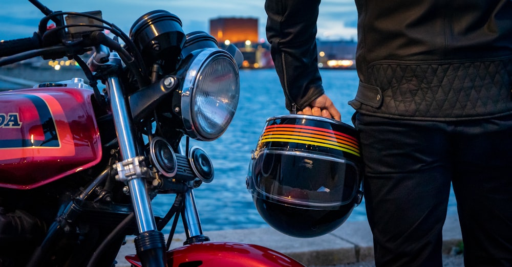 Hombre con chaqueta negra y pantalones negros de pie junto a la motocicleta negra durante el día