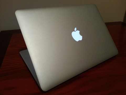 A sleek, silver laptop with a glowing logo on the back, positioned on a dark wooden table. The ambient lighting casts subtle shadows, emphasizing its minimalist design.