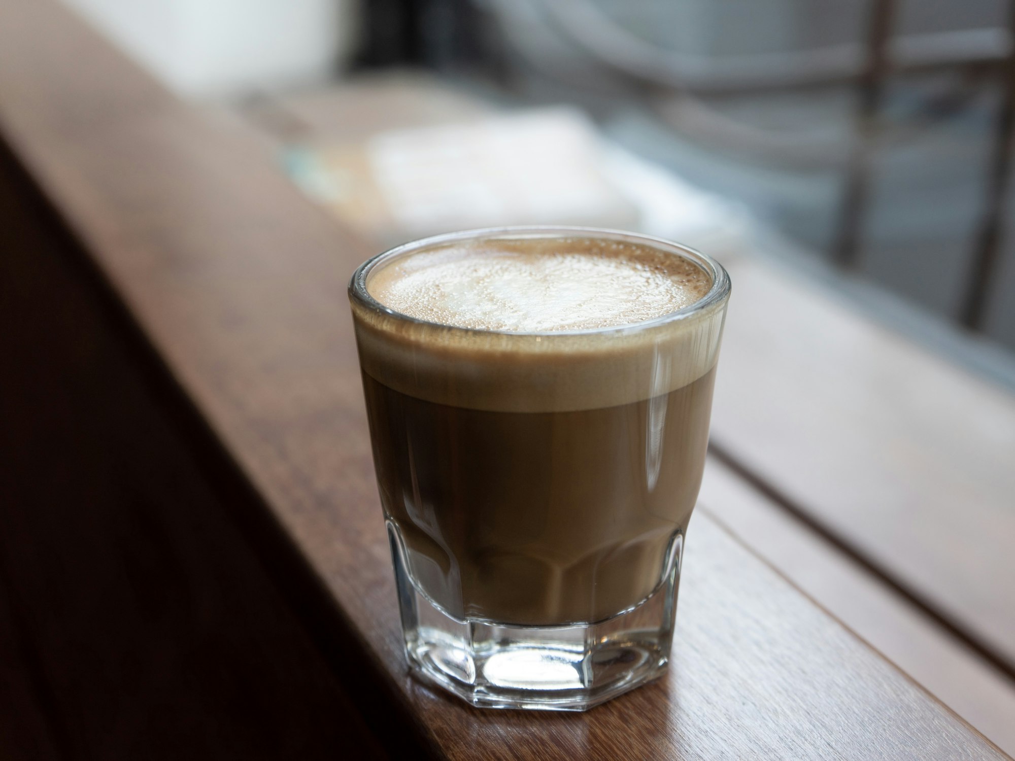 Glass coffee cup on wooden ledge with shallow focus window in background