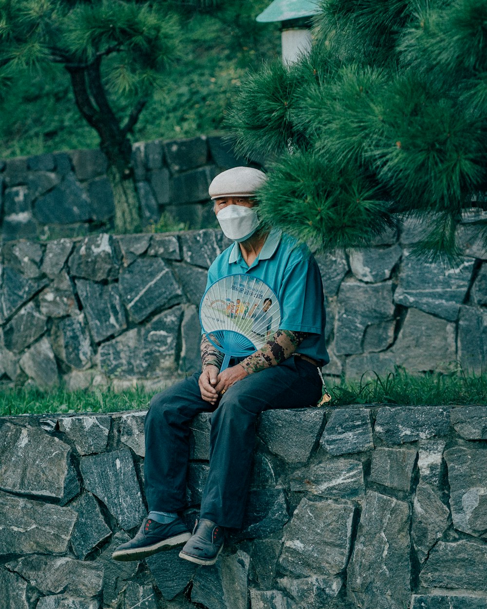 man in blue and red long sleeve shirt and blue denim jeans sitting on gray concrete