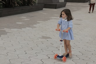 A child gleefully riding a blue and yellow scooter on a smooth pavement