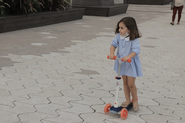 A child gleefully riding a blue and yellow scooter on a smooth pavement