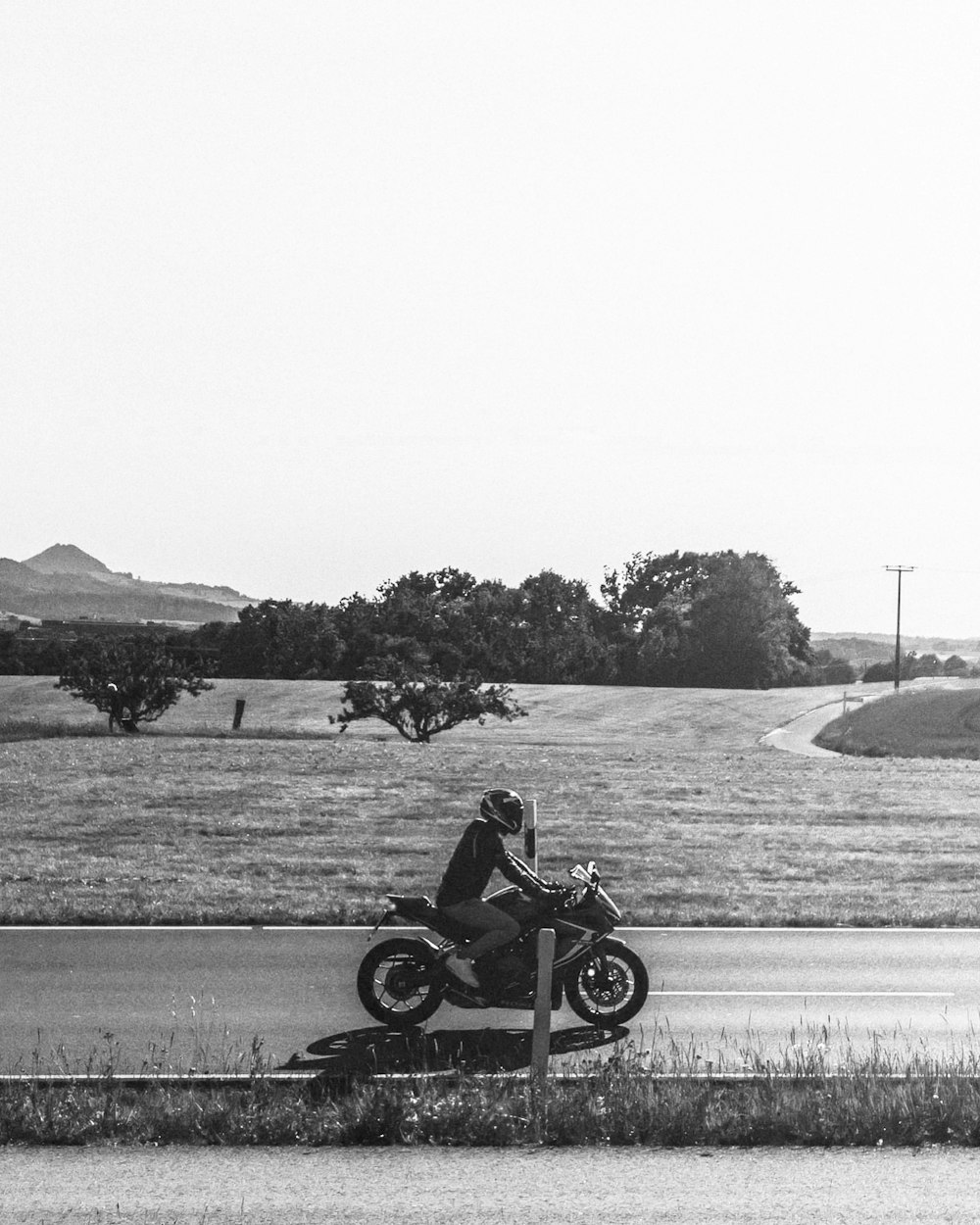 grayscale photo of man riding motorcycle on road