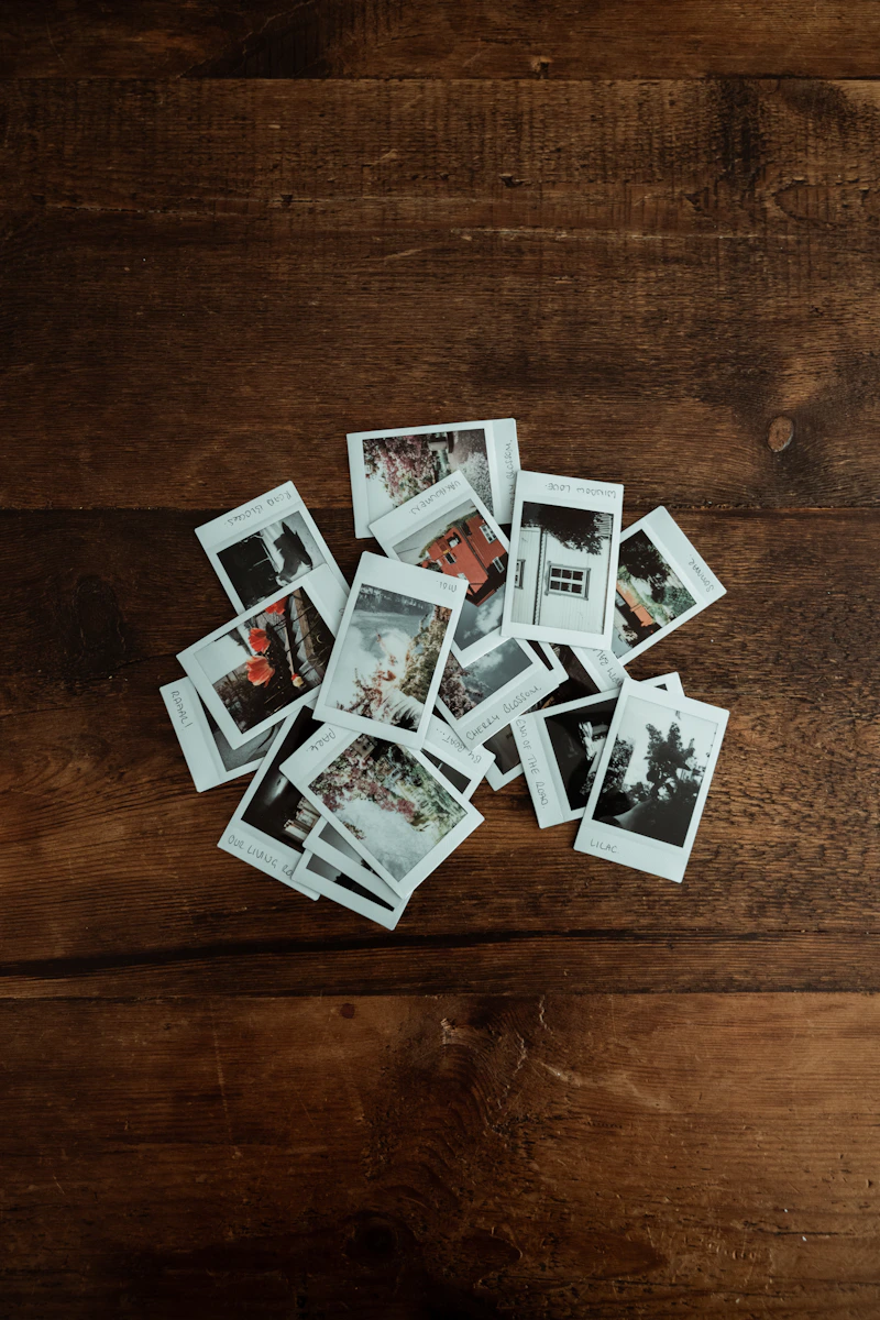 A pile of printed polaroid photos scattered on a wooden table - the kind of memories that get filed away instead of seen