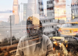 A creative double exposure image featuring a person reading, superimposed with a cityscape of tall, modern buildings. The scene includes a busy urban street with cars, suggesting a bustling city life.