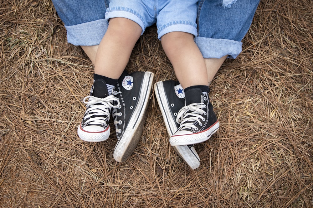 person in blue denim shorts and black and white converse all star high top sneakers