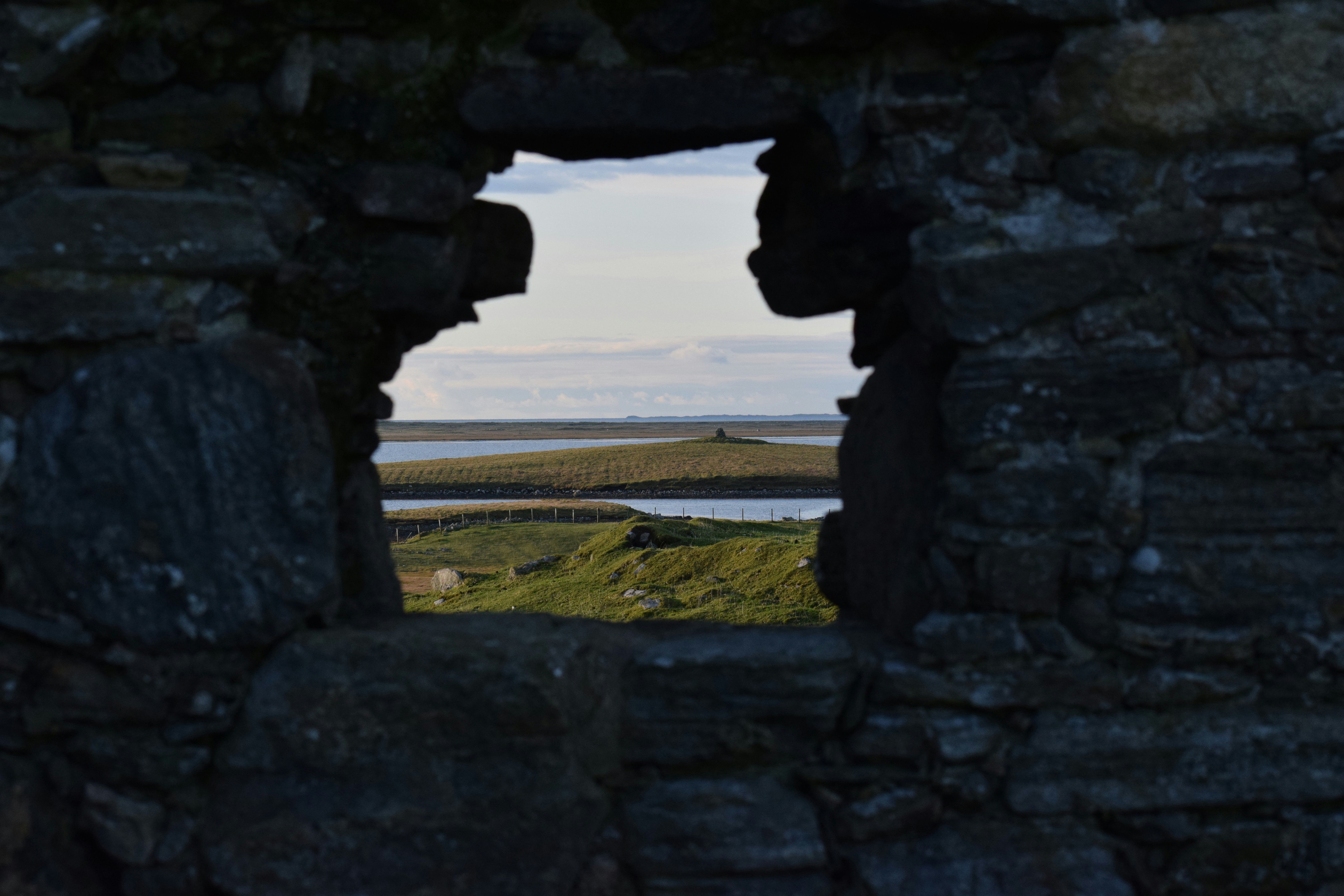 gray concrete arch near body of water during daytime, A view from the ruins of Teampull na Trionaid. 