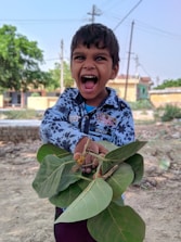 A cheerful child holding a backpack filled with school supplies in a sunny park.